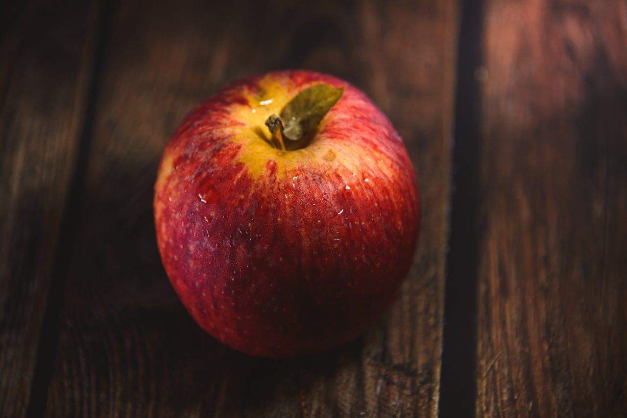 Close-up of a fresh red apple with water droplets on a rustic wooden table, offering a healthy and nutritious look.
