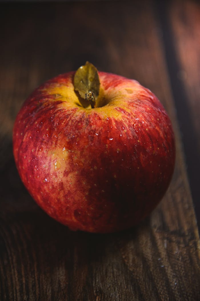 Close-up of a juicy red apple with water droplets on a wooden table, emphasizing freshness and healthy eating.